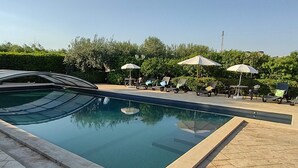A swimming pool with lounge chairs and umbrellas, surrounded by greenery.