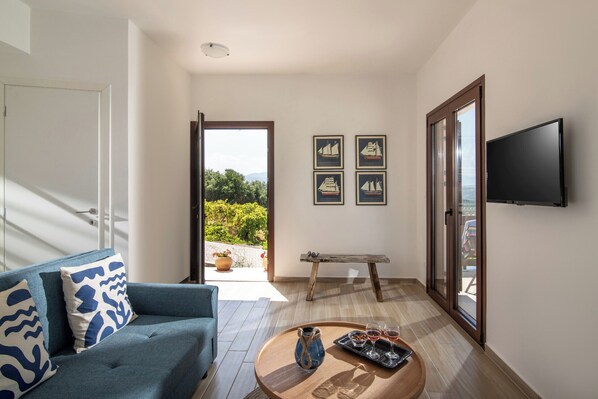 Una sala de estar moderna con un sofá azul, una mesa de centro de madera con bebidas, y un televisor montado en la pared.