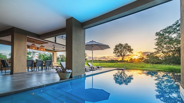 Una piscina infinita con vistas despejadas al atardecer, mobiliario exterior con sombrillas y un diseño arquitectónico moderno.