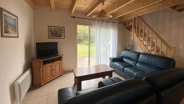 Ein Wohnzimmer mit Holzboden, einem schwarzen Ledersofa, einem HolztV-Schrank und einer Glastür, die in einen Garten führt.
