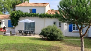 Ein Haus mit Ziegeldach, einer überdachten Terrasse mit Tisch und Stühlen sowie einem kleinen Garten.