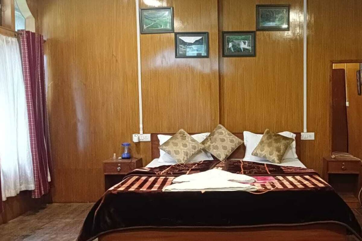 A hotel room with a wooden paneled wall, a bed with patterned pillows, a nightstand with a lamp, and a radiator.