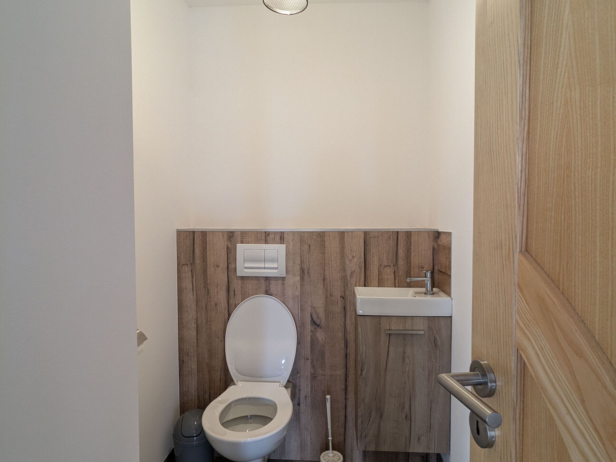Een badkamer met een toilet, een wastafel en een wand van houten panelen.