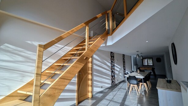 Un interior modern amb una escala de fusta, una zona de menjador i una cuina.