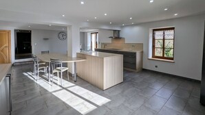 Una cuina moderna amb una illa central, zona de menjador amb cadires i un gran finestral que aporta llum natural.