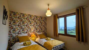 A room with two beds, a floral wallpaper, a window with curtains, and a hanging light fixture.