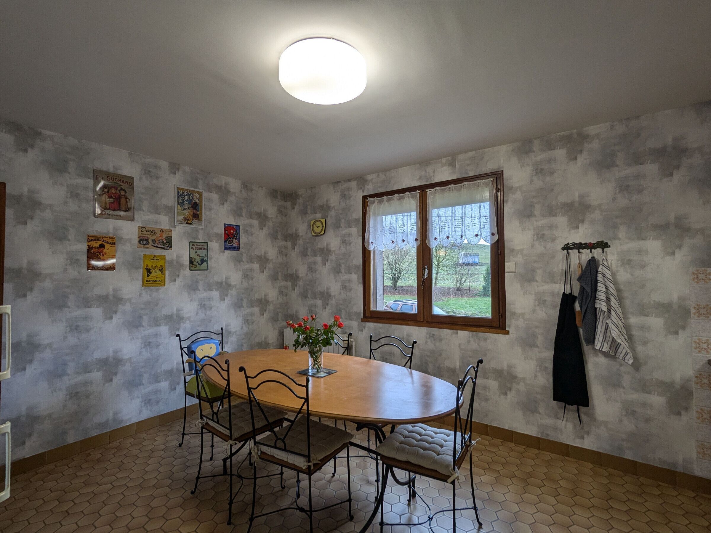 Ein Essbereich mit einem runden Holztisch, vier Stühlen, einem Blumenstrauß und einem Fenster mit Vorhängen.