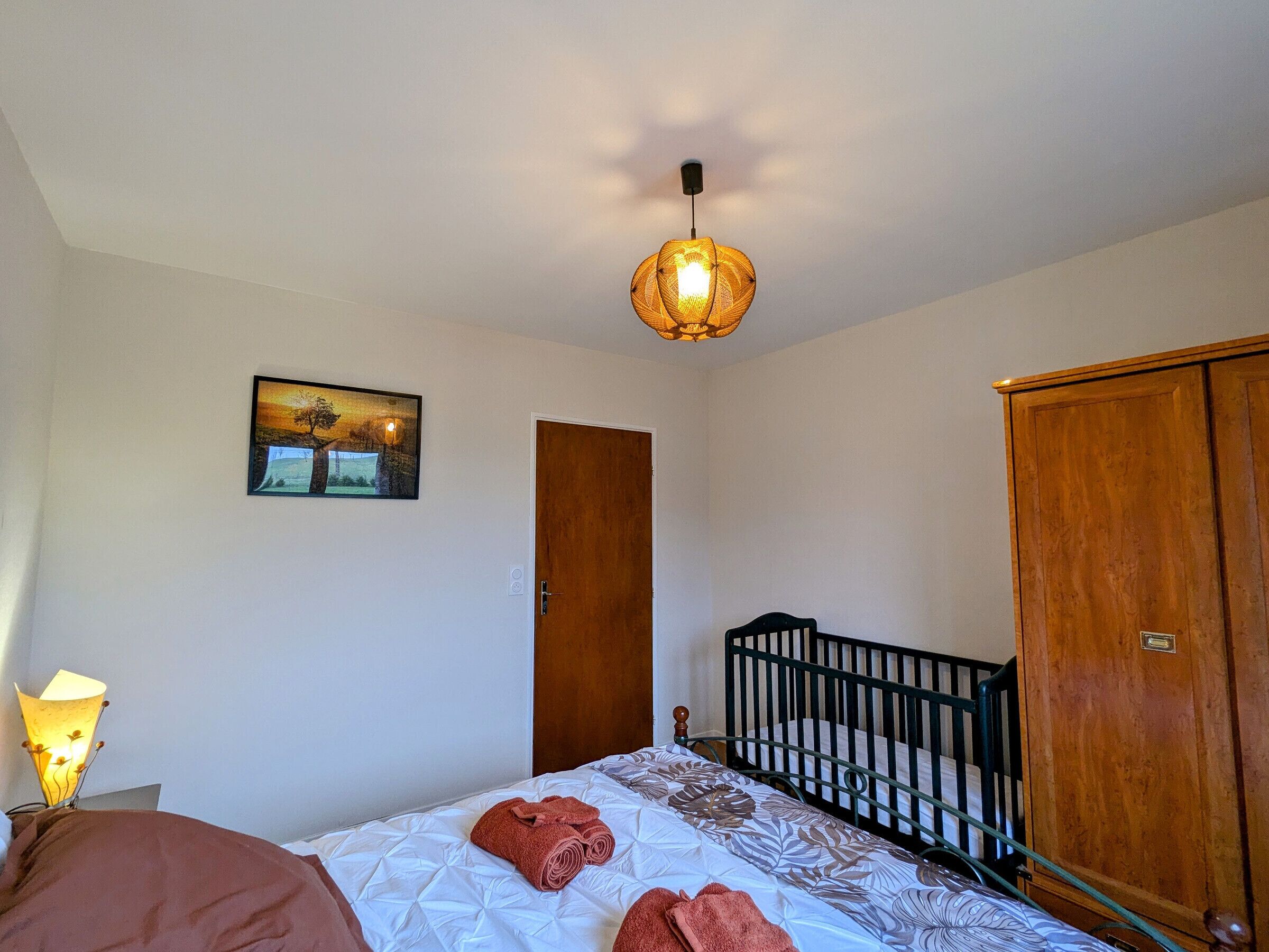 Een slaapkamer met een bed, een houten garderobe, een deur en een aan de muur hangend schilderij.