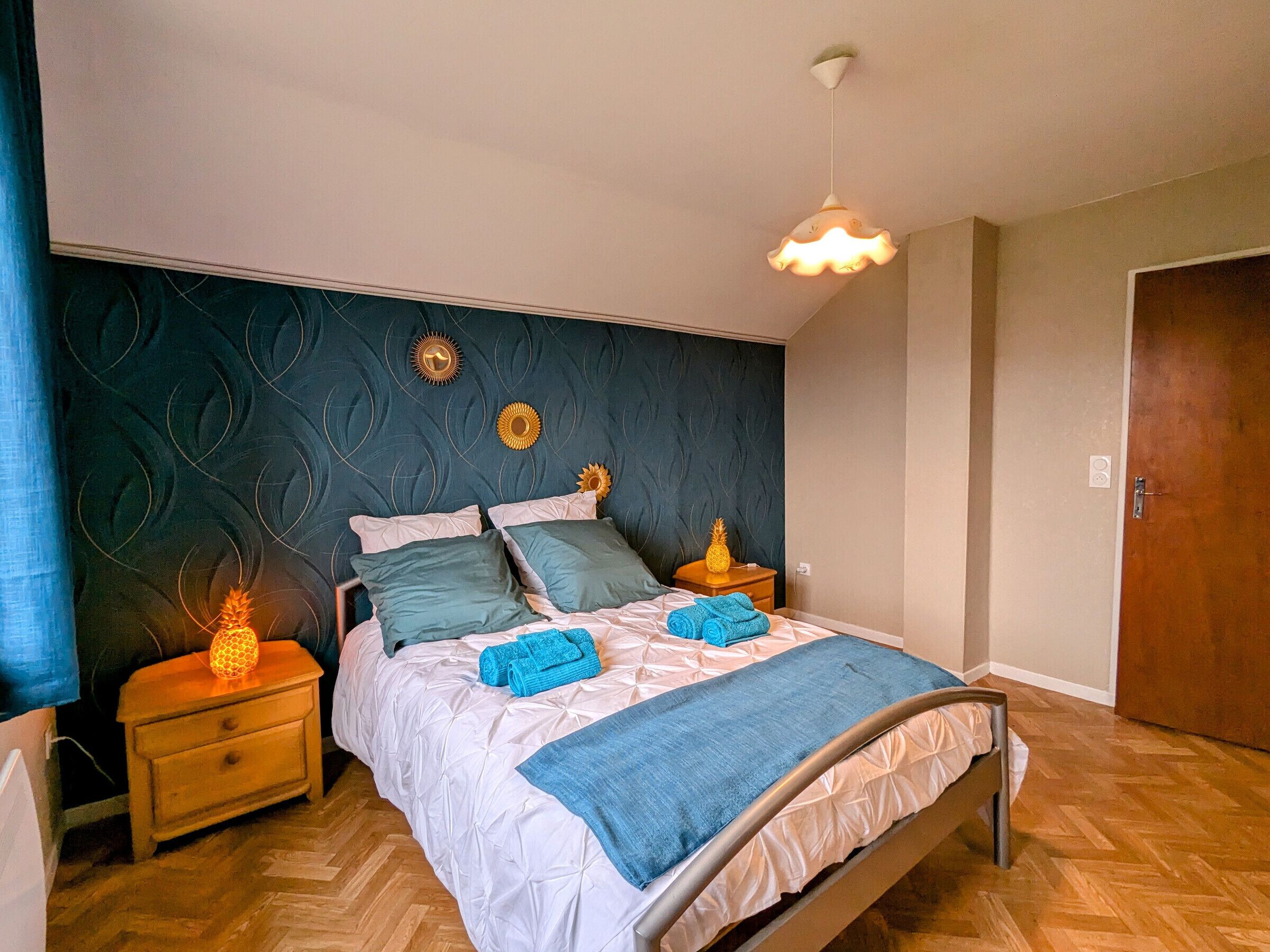 Une chambre à coucher avec un lit, deux tables de chevet, une porte en bois et un mur orné de motifs décoratifs.