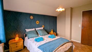 Une chambre à coucher avec un lit, deux tables de chevet, une porte en bois et un mur orné de motifs décoratifs.