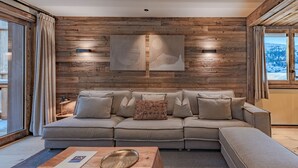 Una sala de estar moderna con un panel de madera, un sofá seccional, una mesa de centro y vistas a un paisaje nevado a través de amplios ventanales.