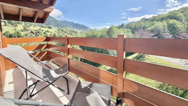 A wooden balcony with a view of a green valley and mountains.