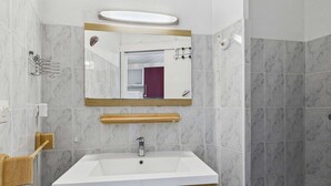 Une salle de bain avec un lavabo blanc, un miroir et un espace douche.