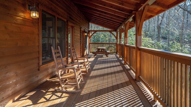 Une cabane en bois dotée d’un porche couvert, de chaises en bois, d’une table et offrant une vue sur la forêt.