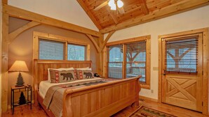 Une chambre à coucher en bois, avec un lit, des fenêtres, une porte et un ventilateur de plafond.