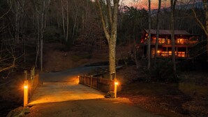 Un pont en bois menant à un chalet à plusieurs niveaux, entouré d’arbres.