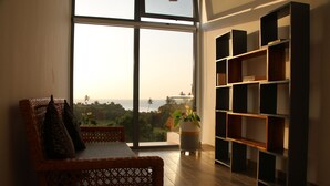 A room with a large window, a wicker sofa, and a bookshelf.