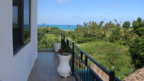 A balcony with a view of a beach and lush greenery.