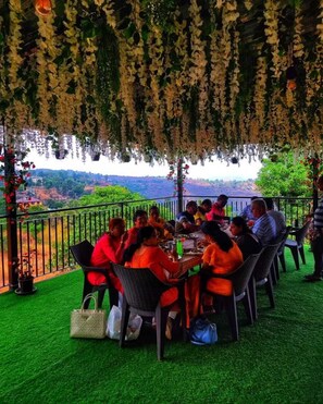 A group of people dining at an outdoor table with a view of a hilly landscape. - Nature Nest Valley Resort (Mahabaleshwar)