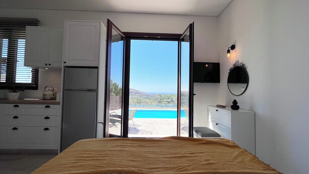 Un dormitorio con cama, vista a una piscina y zona de cocina.