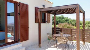 Un porche cubierto con una pérgola de madera, sillas de mimbre y una mesa.