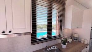 Una cocina moderna con un lavamanos de acero inoxidable, armarios blancos y una ventana con persianas.