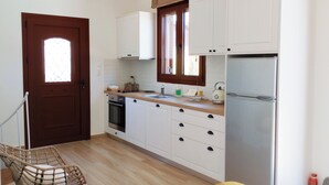 Una cocina con armarios blancos, un refrigerador de acero inoxidable, una puerta de madera y una silla de mimbre.