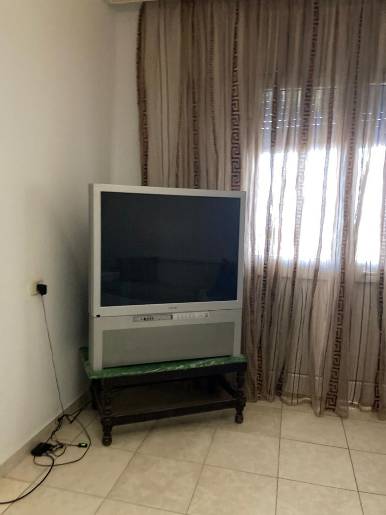 Un téléviseur posé sur un meuble dans une pièce où se trouvent un rideau et une fenêtre.