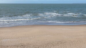 Een strand met een breed zandstrand en rustige golven.