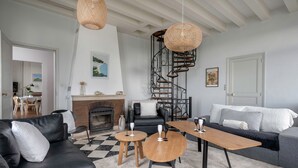 Een moderne woonkamer met een open haard, een zwarte leren bank, een grijze bank, een houten salontafel en een zwart-wit geruit tapijt.