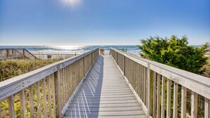 Un muelle de madera que conduce a una playa con cielo despejado y sol brillante.