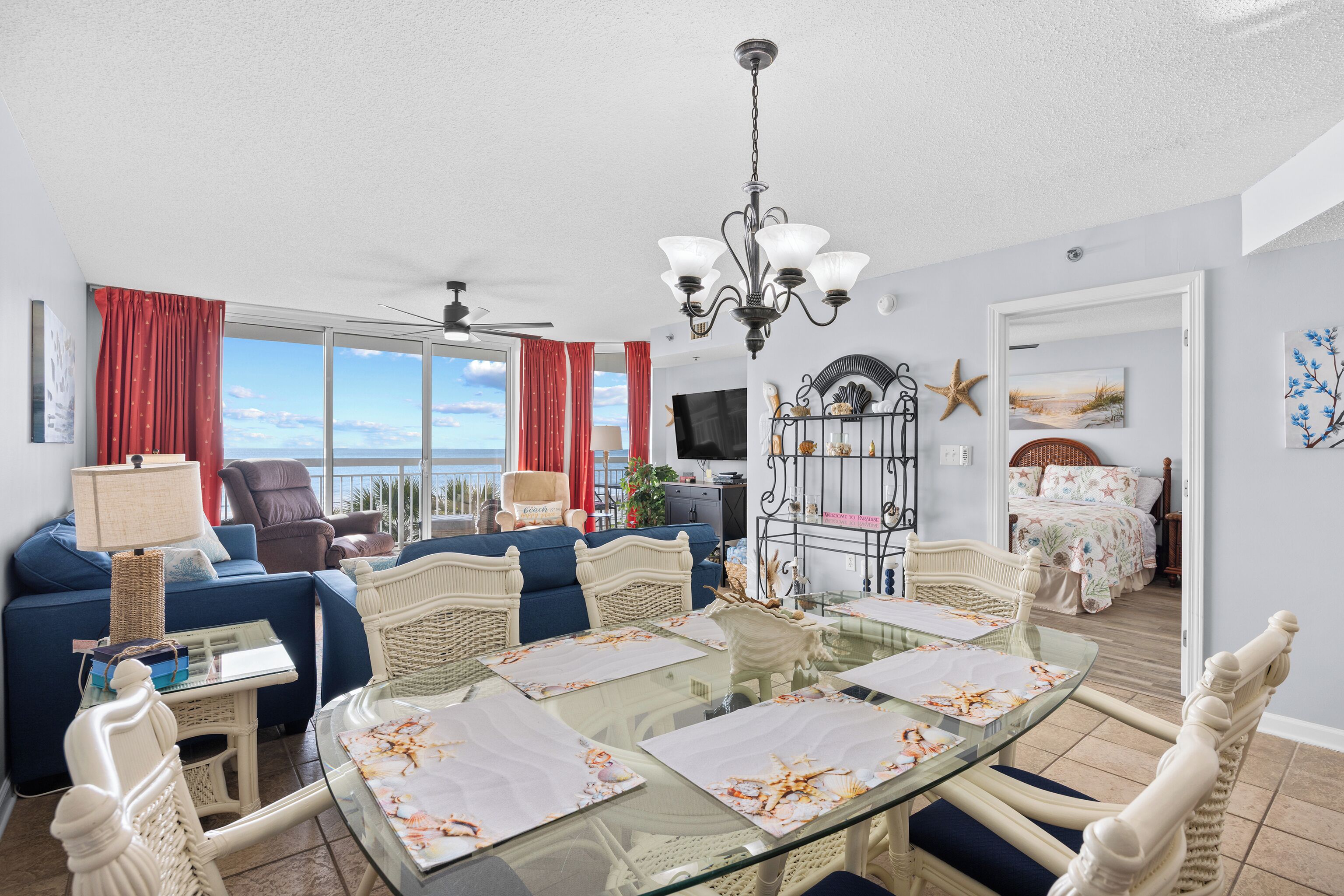 A spacious living room with a glass dining table, blue sofa, and a view of the ocean.