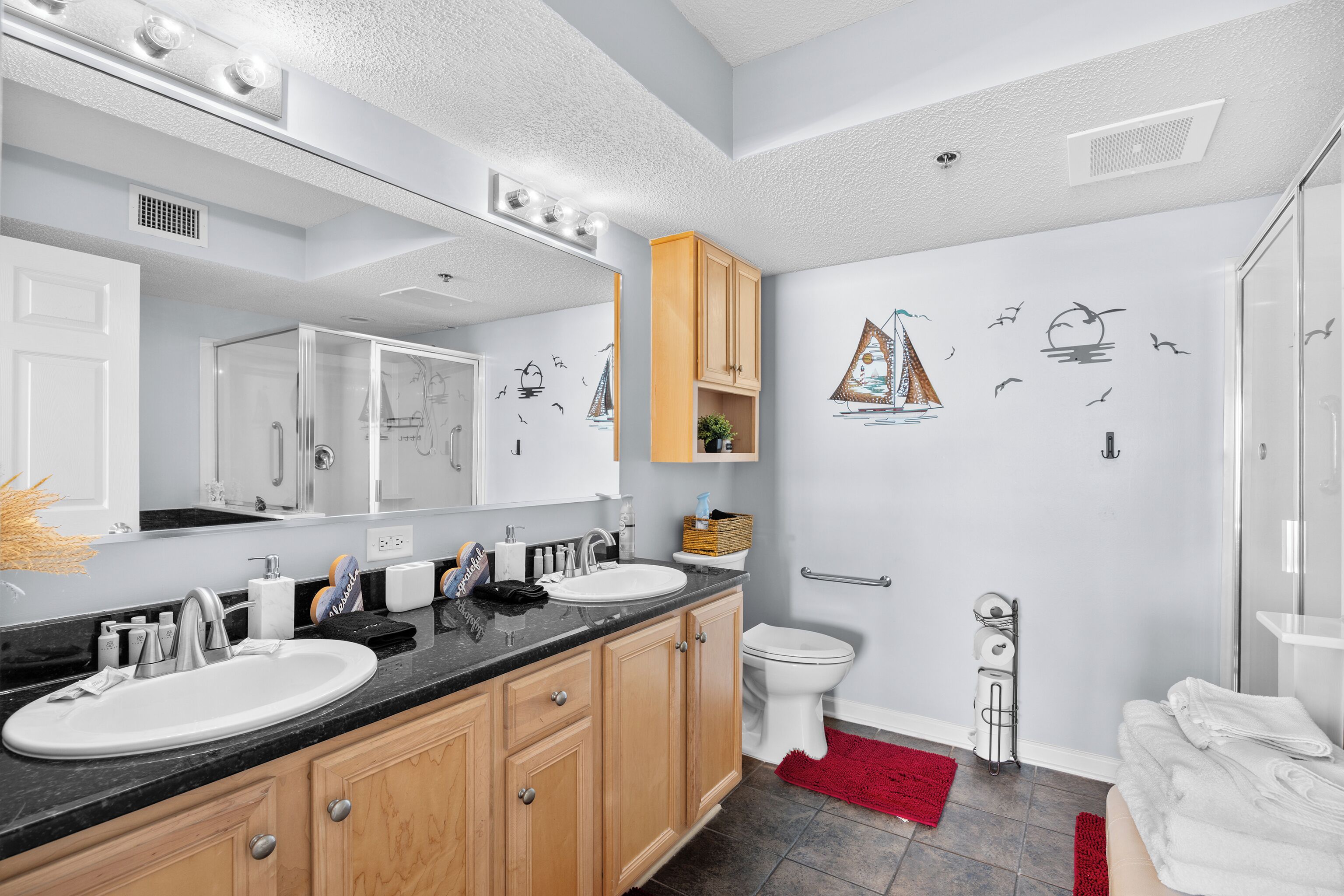 A modern bathroom with two sinks, a large mirror, wooden cabinets, a toilet, and a shower area.