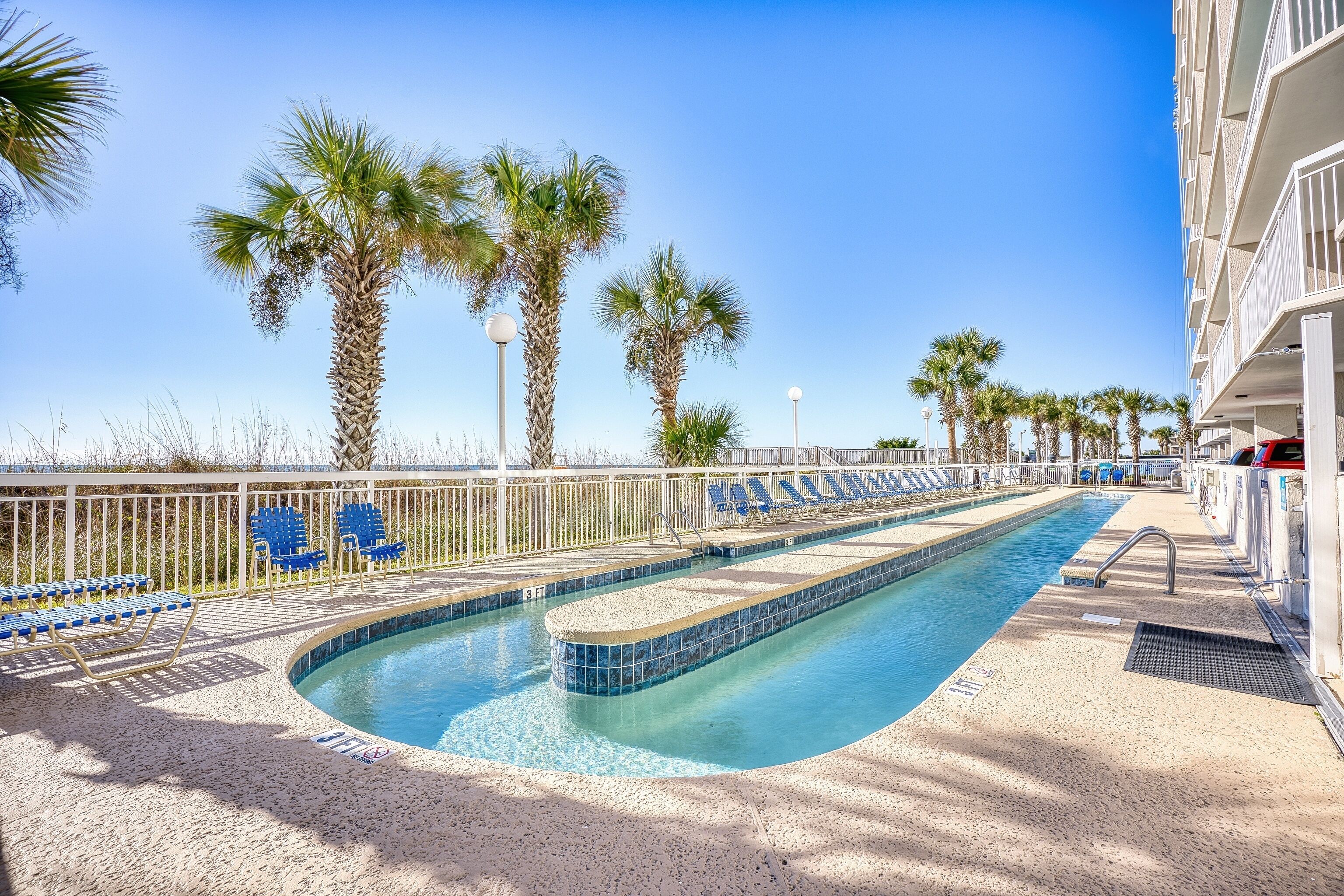 An outdoor swimming pool with blue chairs and palm trees.