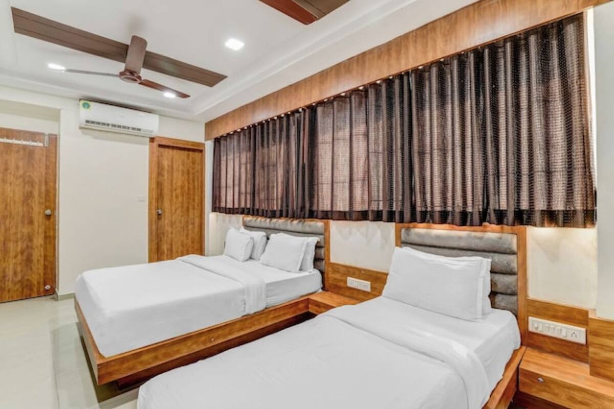 Habitación de hotel con dos camas individuales, ventilador de techo, equipo de aire acondicionado y un ventanal con cortinas.