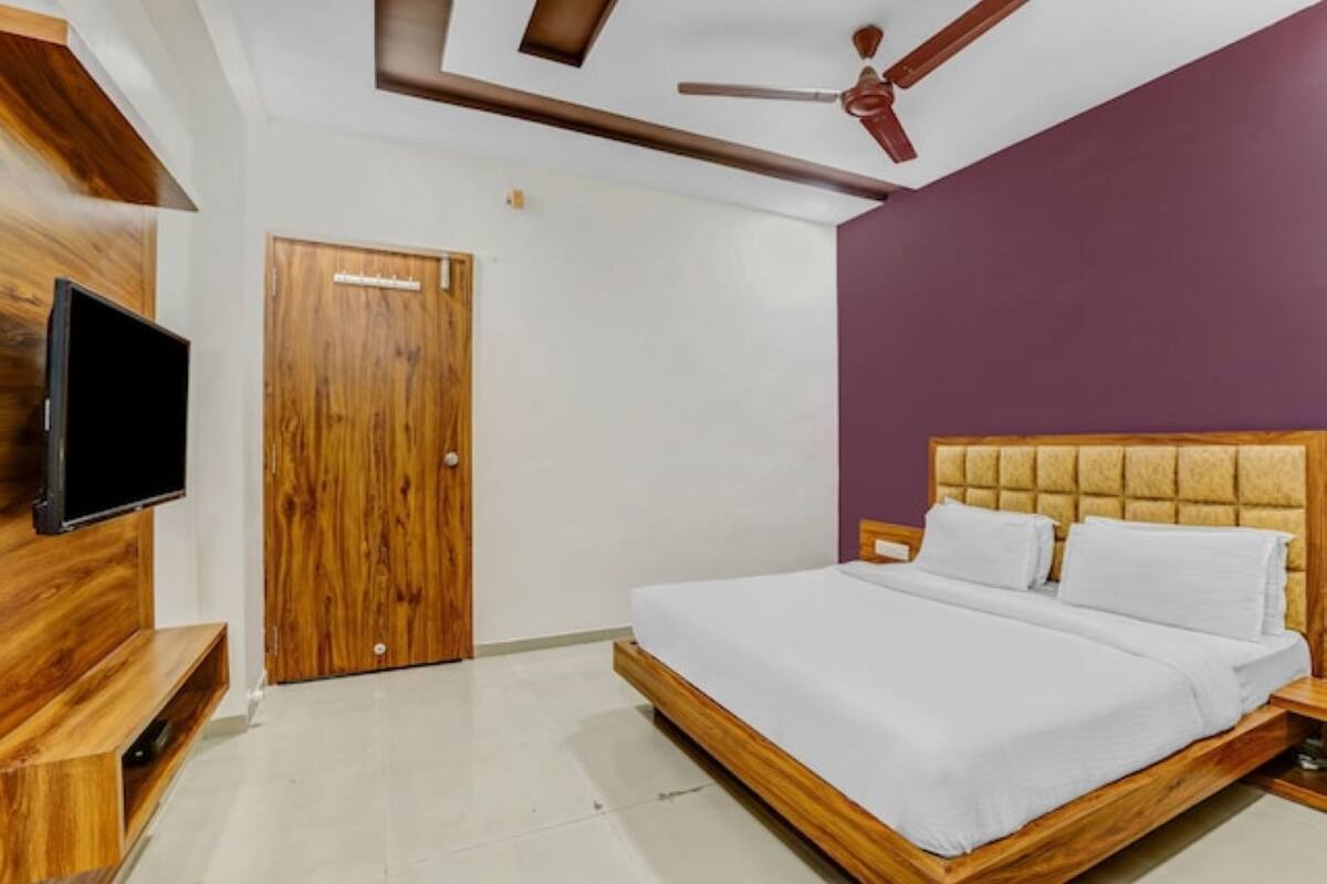 Un dormitorio con estructura de cama de madera, televisor de pantalla plana en la pared y ventilador de techo.