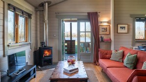 Een gezellige woonkamer met een open haard, een bank, een bijzettafeltje met boeken en uitzicht op de omgeving.