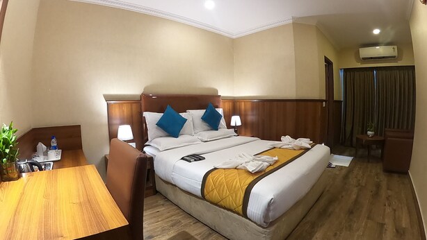 A hotel room with a bed, bedside tables, a desk, a chair, a ceiling fan, and an air conditioning unit. - Hotel Noor Empire International (Bengaluru)