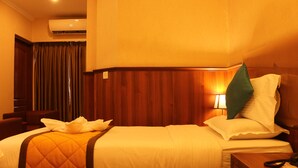 A hotel room with two beds, a wooden headboard, a green pillow, a bedside lamp, and an air conditioning unit. - Hotel Noor Empire International (Bengaluru)