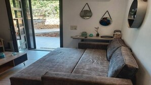 Un salon moderne avec un canapé gris, une petite table et un banc. On y trouve deux miroirs fixés au mur et une étagère ornée d’objets décoratifs.