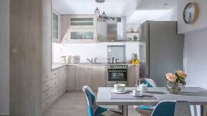 Une cuisine moderne avec des meubles de couleur bois clair, un îlot central et un coin repas avec des chaises bleues.