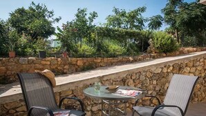 Un espace extérieur aménagé en terrasse, avec deux chaises et une table, entouré d’un mur de pierre et d’une végétation luxuriante.