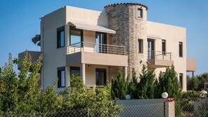 Une maison moderne à deux étages, dotée d’une tour en pierre, de balcons et d’une cour clôturée.