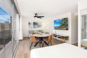 A modern hotel room with a balcony, a dining area, and a large TV.