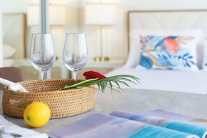A hotel room with a bed, a bedside table with two glasses and a basket, and a pillow with a floral design.
