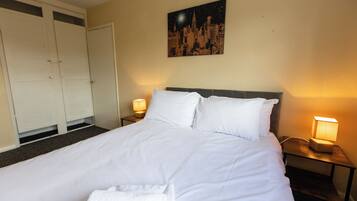 A neatly made bed with white linens, a nightstand with a lamp, and a cityscape painting on the wall.