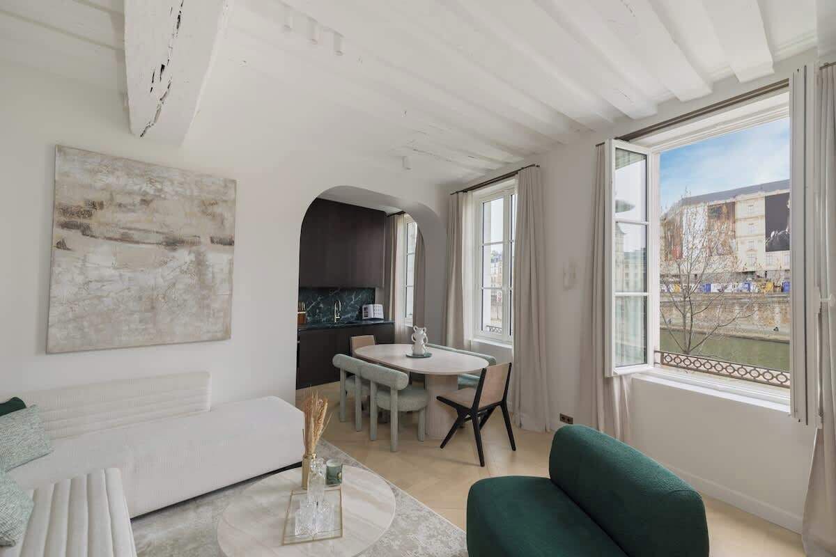 Een moderne woonkamer met een witte bank, een ronde salontafel en een groene fauteuil. Er is een eethoek met een witte tafel en stoelen, en een keuken is zichtbaar door een boog.