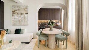 Un salon moderne avec une table ronde, des fauteuils à revêtement vert, un canapé blanc et un grand tableau abstrait accroché au mur.