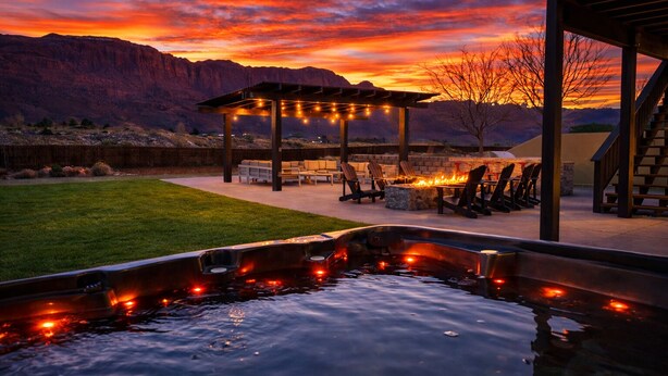 Un jacuzzi iluminado, un espacio de estar techado y el paisaje de montañas al fondo.