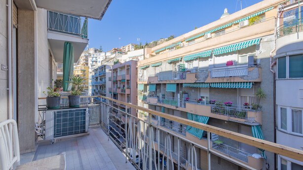 Un edificio residencial de varios pisos con balcones, mobiliario exterior y plantas en macetas.